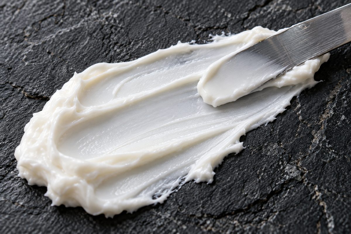 Dense white ceramide cream swatched across dark slate with a laboratory spatula