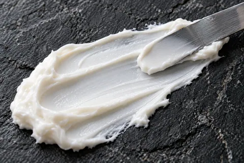Dense white ceramide cream swatched across dark slate with a laboratory spatula